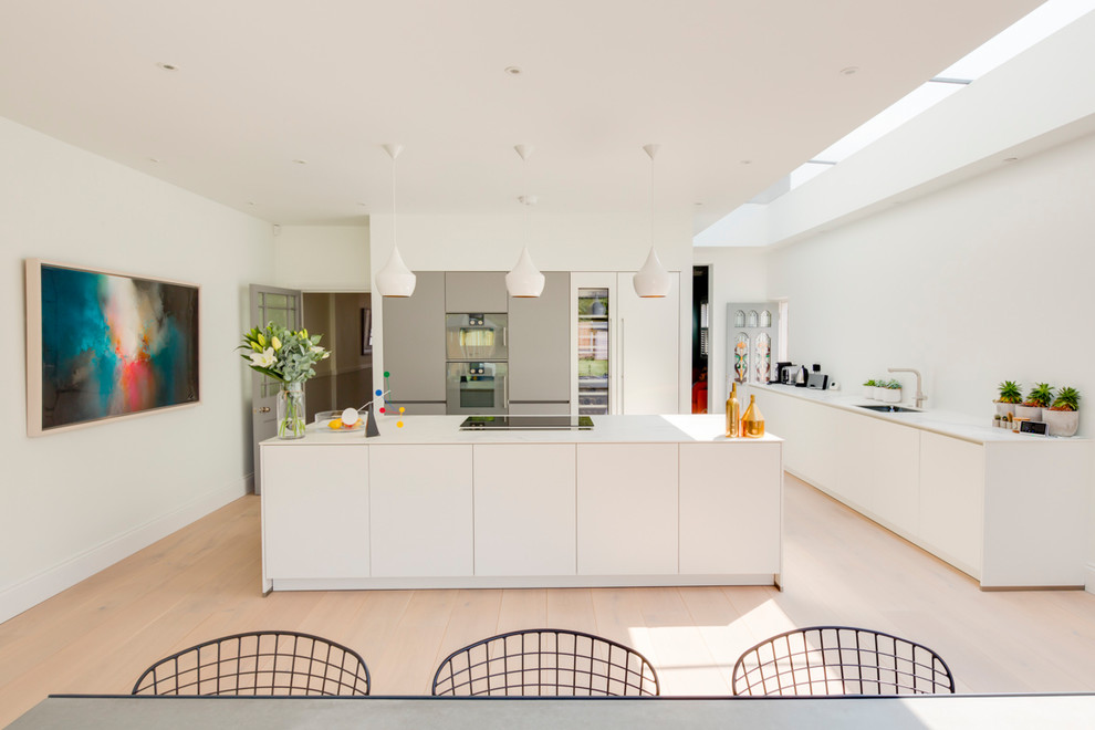 Large contemporary eat-in kitchen in London with an undermount sink, flat-panel cabinets, white cabinets, stainless steel appliances, with island, beige floor and white benchtop.