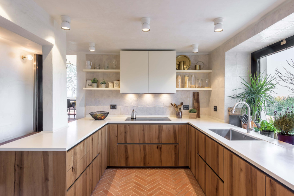 Photo of a mediterranean u-shaped kitchen in Florence with a single-bowl sink, flat-panel cabinets, medium wood cabinets, grey splashback, a peninsula, orange floor and white benchtop.