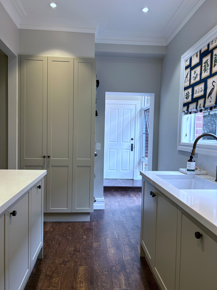 This is an example of a large modern galley dedicated laundry room in Sydney with an undermount sink, shaker cabinets, green cabinets, marble benchtops, grey splashback, engineered quartz splashback, green walls, dark hardwood floors, a stacked washer and dryer, brown floor, grey benchtop and coffered.