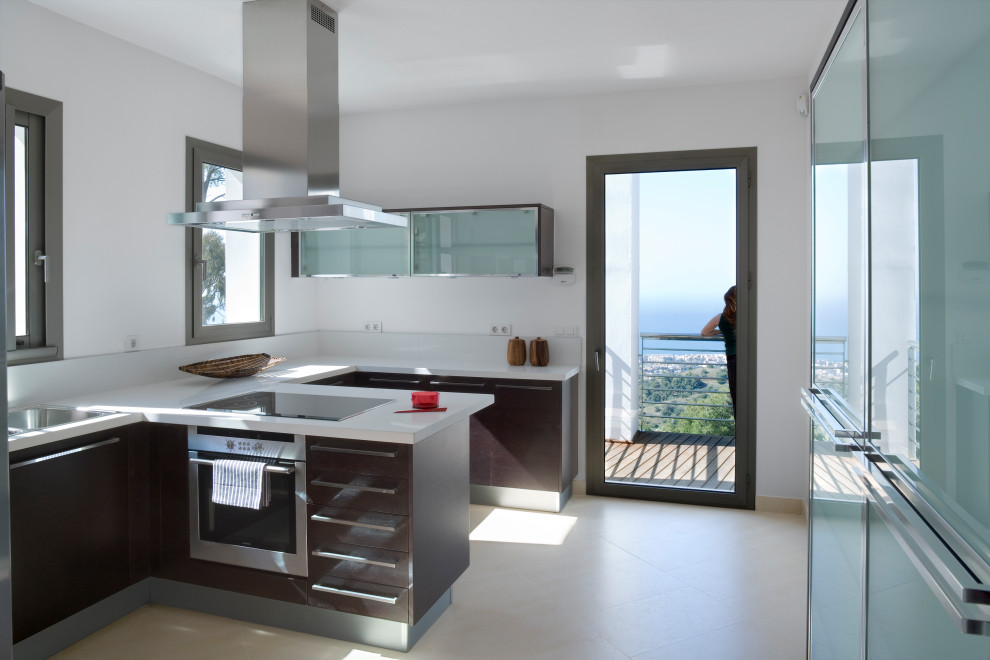 Large contemporary u-shaped separate kitchen in Malaga with a drop-in sink, dark wood cabinets, marble benchtops, white splashback, marble splashback, stainless steel appliances, marble floors, with island and beige floor.