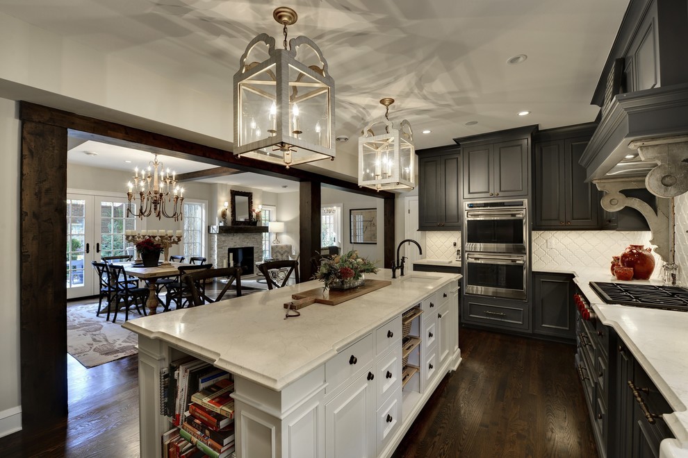 Large traditional u-shaped eat-in kitchen in Minneapolis with raised-panel cabinets, grey cabinets, white splashback, stainless steel appliances, dark hardwood floors, with island, brown floor, a farmhouse sink, solid surface benchtops and glass tile splashback.
