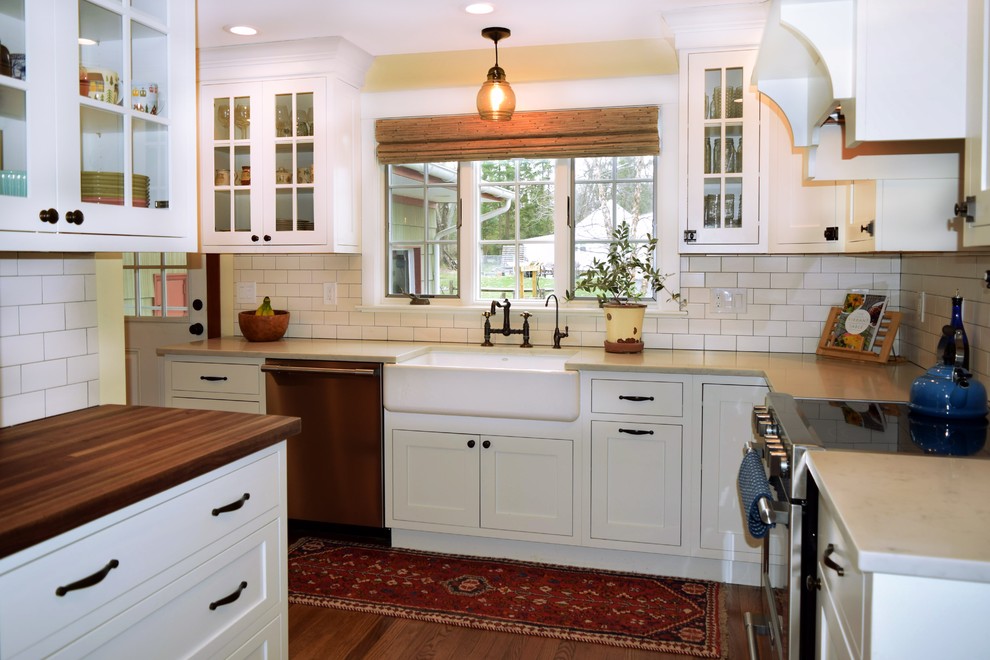 This is an example of a mid-sized arts and crafts l-shaped separate kitchen in Philadelphia with a farmhouse sink, shaker cabinets, white cabinets, quartzite benchtops, subway tile splashback, stainless steel appliances, medium hardwood floors, brown floor, white splashback, grey benchtop and no island.