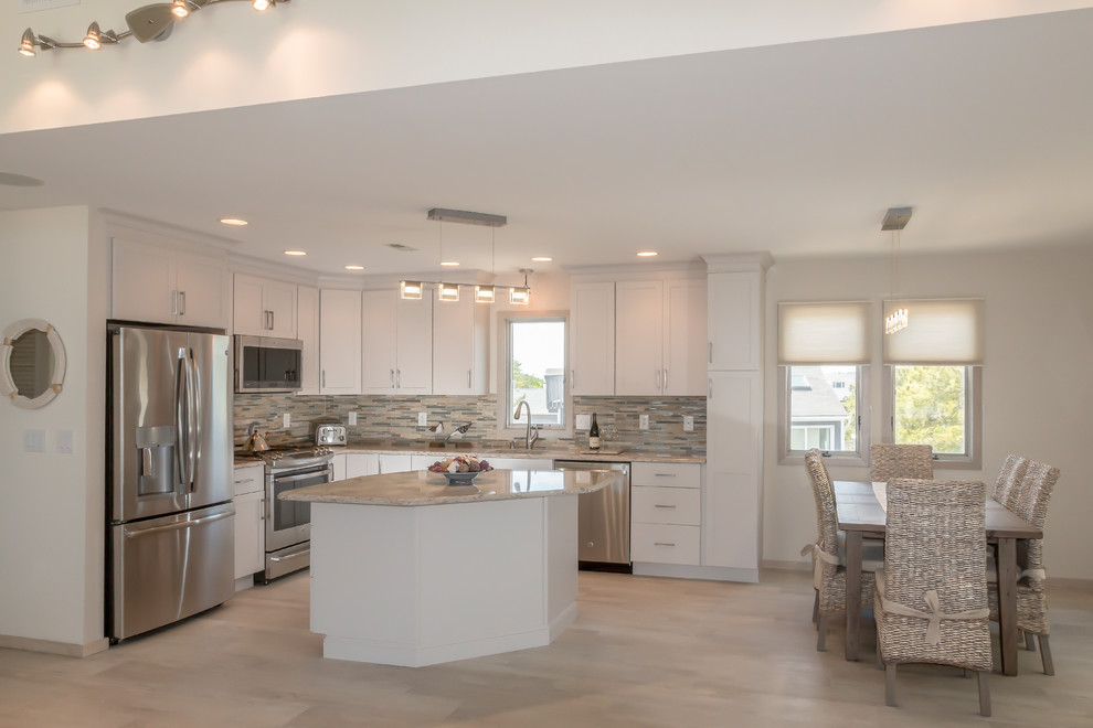 Large transitional l-shaped open plan kitchen in New York with a drop-in sink, recessed-panel cabinets, white cabinets, granite benchtops, metallic splashback, stone tile splashback, stainless steel appliances, ceramic floors, with island and beige floor.