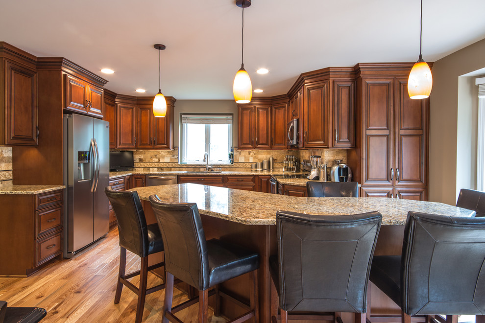 This is an example of a large traditional u-shaped eat-in kitchen in Detroit with an undermount sink, raised-panel cabinets, medium wood cabinets, granite benchtops, beige splashback, subway tile splashback, stainless steel appliances, light hardwood floors and with island.