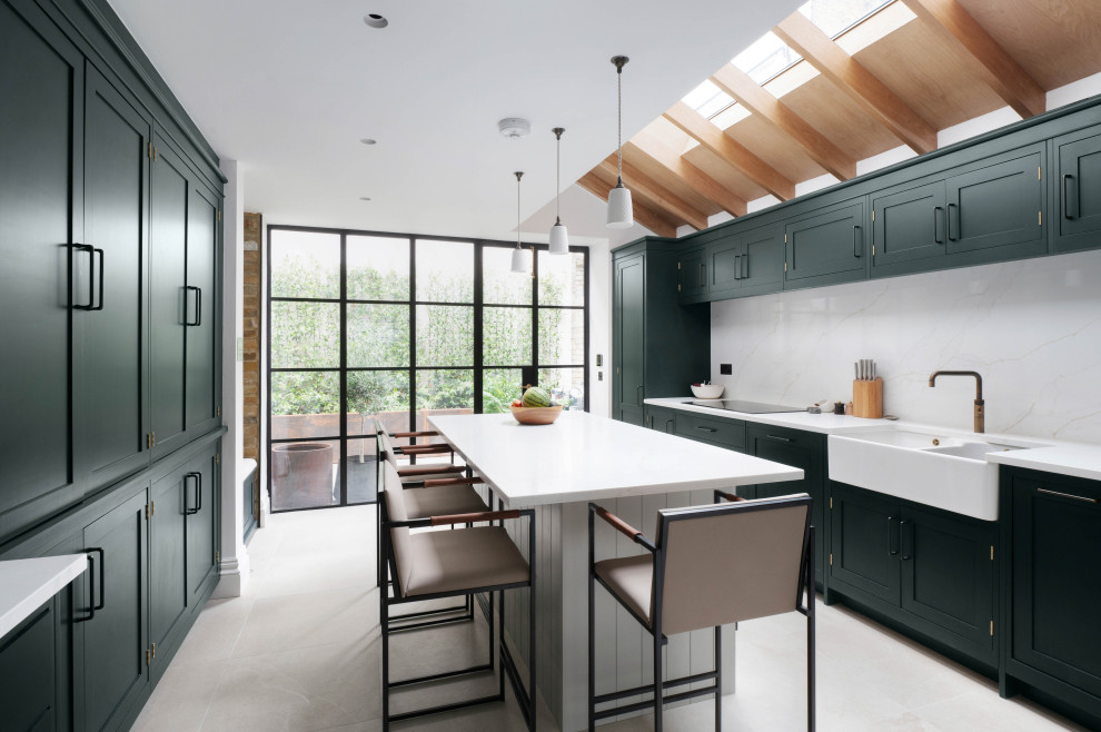 Classic kitchen in London with shaker cabinets, green cabinets, white splashback, an island, white worktops and exposed beams.