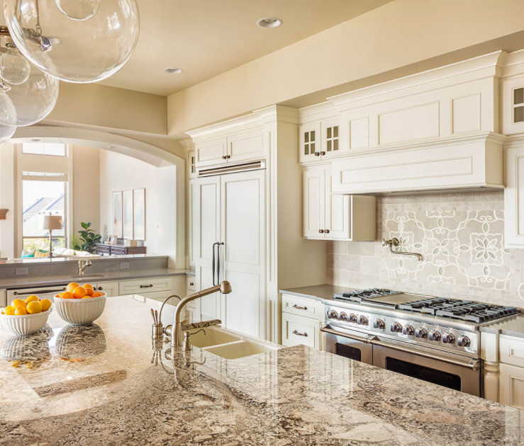 Kitchen - mid-sized transitional kitchen idea in Los Angeles with a farmhouse sink, recessed-panel cabinets, white cabinets, granite countertops, beige backsplash, stone tile backsplash, stainless steel appliances and an island