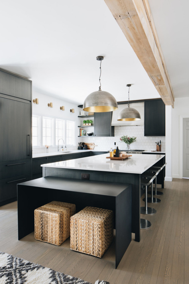 Inspiration for a large contemporary l-shaped kitchen in Los Angeles with an undermount sink, flat-panel cabinets, black cabinets, quartz benchtops, white splashback, porcelain splashback, panelled appliances, medium hardwood floors, with island, brown floor, white benchtop and exposed beam.