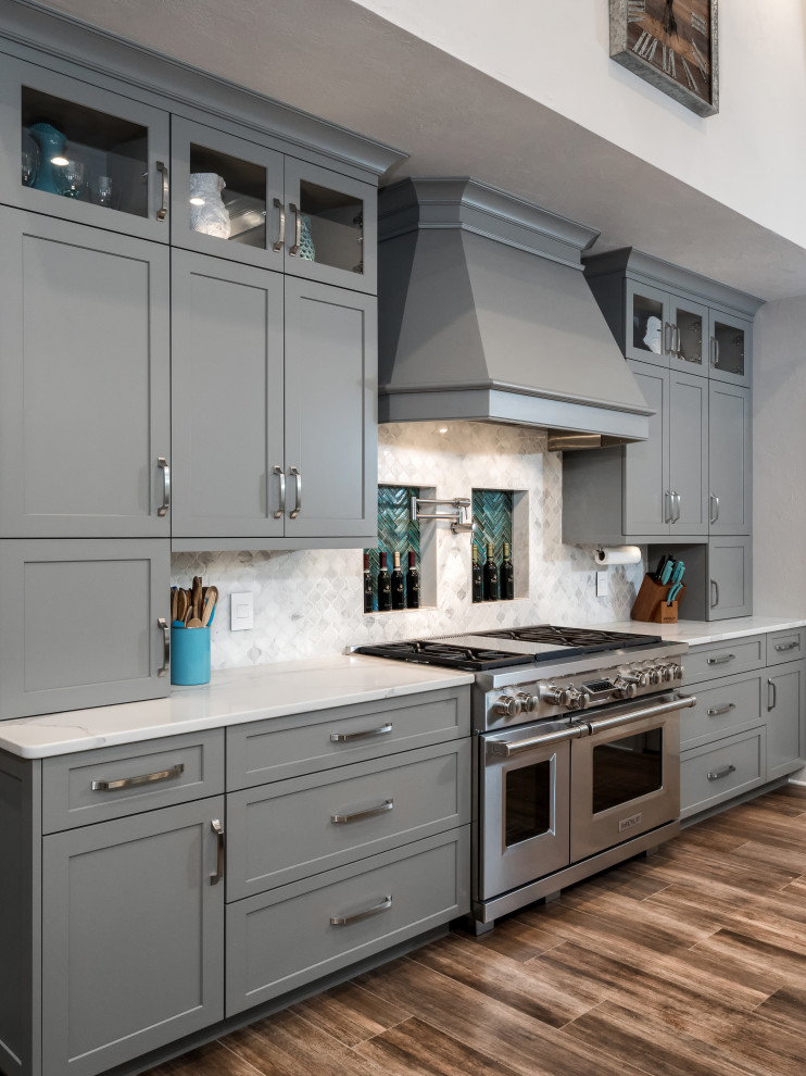 Design ideas for a large transitional l-shaped eat-in kitchen in Miami with a farmhouse sink, shaker cabinets, grey cabinets, quartz benchtops, grey splashback, glass sheet splashback, stainless steel appliances, ceramic floors, with island, brown floor and white benchtop.