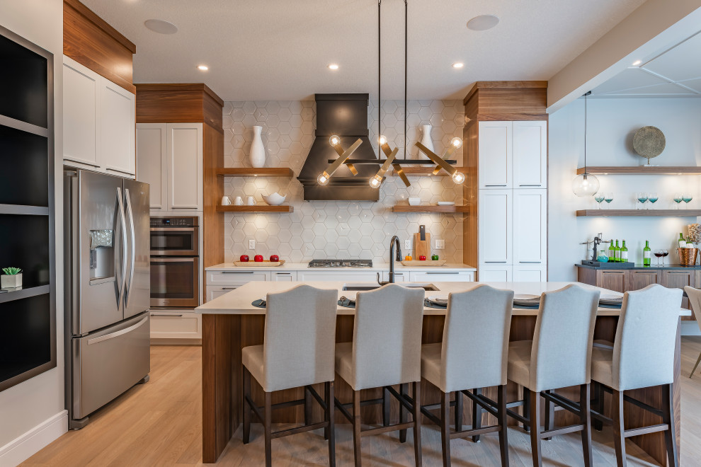 Example of a transitional medium tone wood floor and gray floor eat-in kitchen design in Edmonton with an undermount sink, shaker cabinets, white cabinets, white backsplash, stainless steel appliances, an island and white countertops