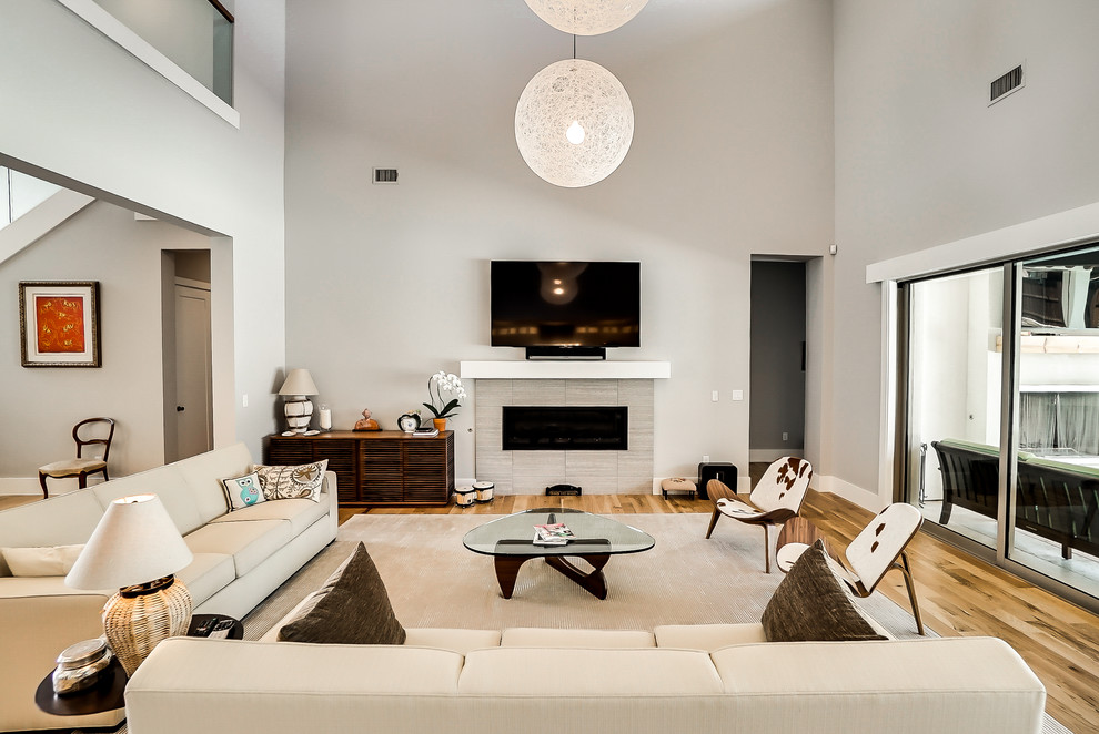 Photo of a large contemporary open concept living room in Dallas with grey walls, light hardwood floors, a standard fireplace, a tile fireplace surround and a wall-mounted tv.