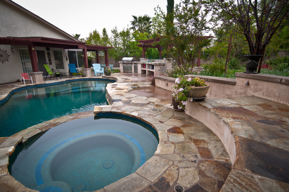 Design ideas for a large eclectic backyard custom-shaped natural pool in Los Angeles with a hot tub and natural stone pavers.