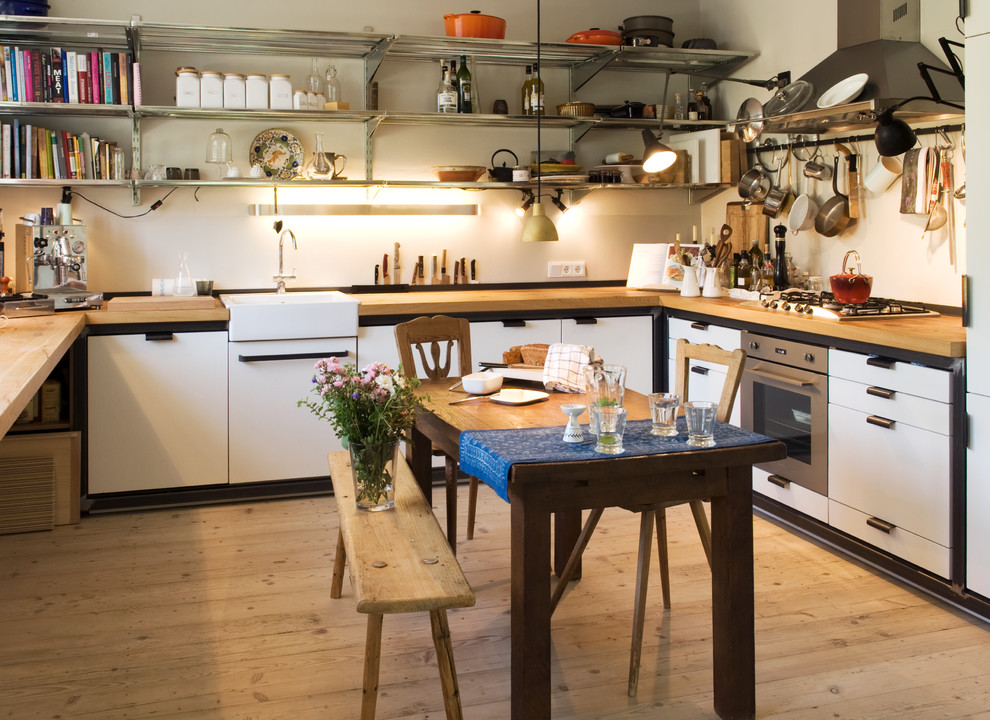 Large country u-shaped eat-in kitchen in Munich with a farmhouse sink, flat-panel cabinets, white cabinets, wood benchtops, white splashback, panelled appliances, medium hardwood floors and no island.
