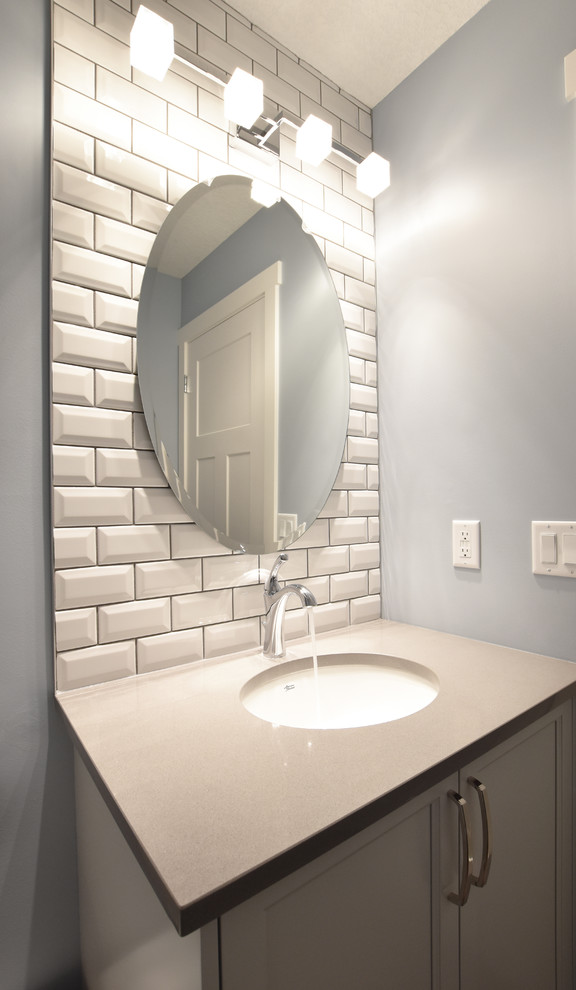 Photo of a mid-sized transitional powder room in Calgary with recessed-panel cabinets, white cabinets, white tile, ceramic tile, blue walls, medium hardwood floors, an undermount sink, solid surface benchtops, a two-piece toilet and brown floor.