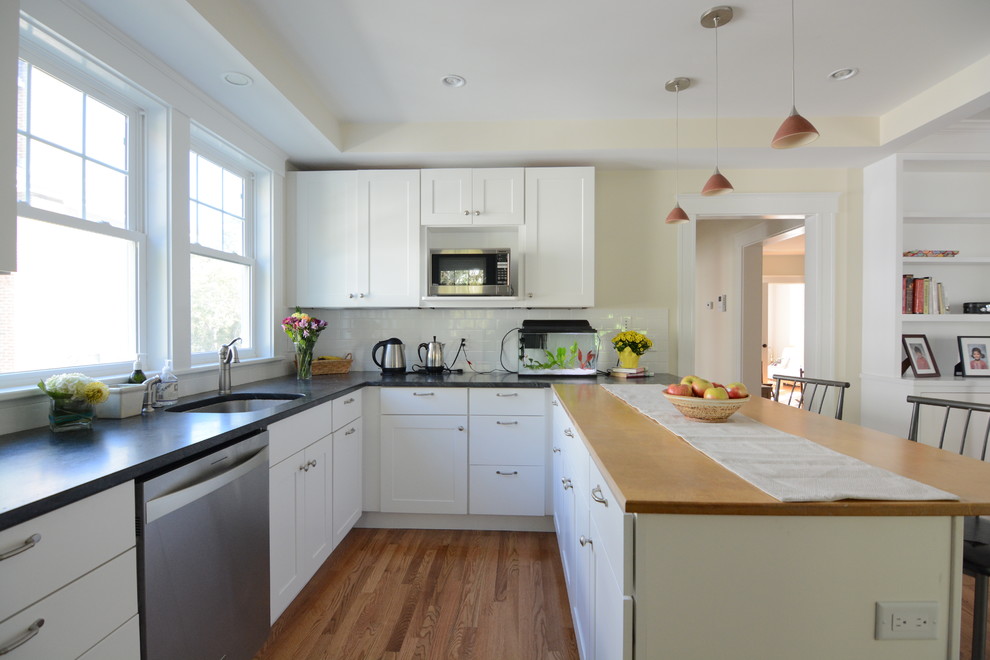 Inspiration for a large transitional l-shaped medium tone wood floor and brown floor kitchen pantry remodel in Boston with a drop-in sink, flat-panel cabinets, white cabinets, solid surface countertops, white backsplash, subway tile backsplash, stainless steel appliances and an island