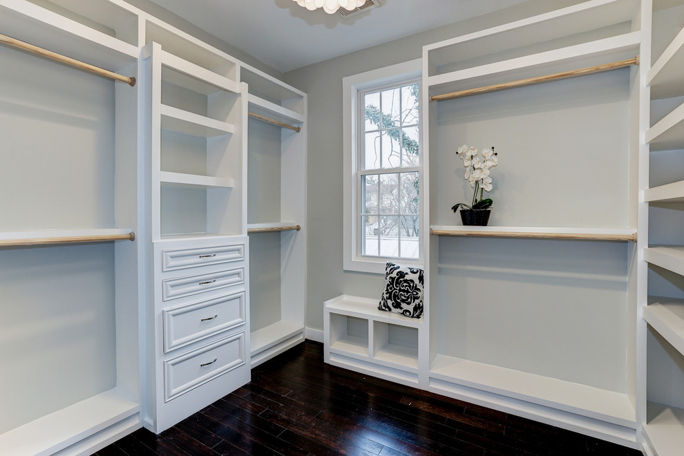 This is an example of a mid-sized traditional women's dressing room in DC Metro with recessed-panel cabinets, white cabinets and dark hardwood floors.