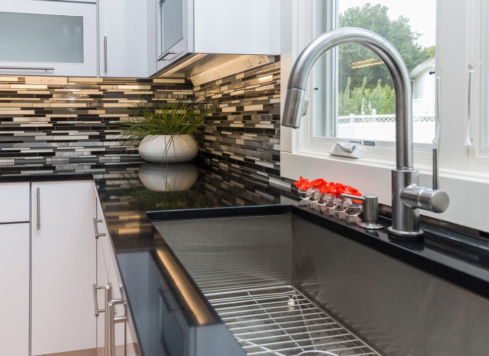 Large trendy u-shaped light wood floor open concept kitchen photo with an undermount sink, flat-panel cabinets, white cabinets, granite countertops, multicolored backsplash, mosaic tile backsplash, stainless steel appliances and an island