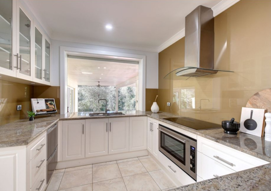Large traditional u-shaped kitchen in Adelaide with a double-bowl sink, glass-front cabinets, white cabinets, granite benchtops, brown splashback, glass sheet splashback, stainless steel appliances, porcelain floors, with island, beige floor and brown benchtop.