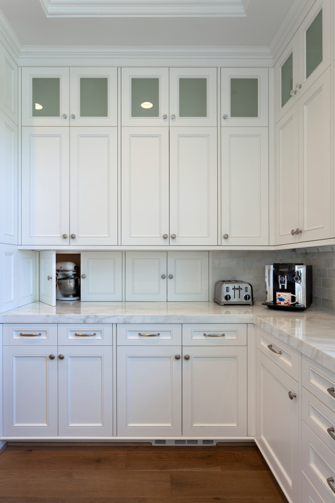 Foto på ett mycket stort vintage vit kök, med en undermonterad diskho, luckor med upphöjd panel, vita skåp, marmorbänkskiva, vitt stänkskydd, stänkskydd i marmor, rostfria vitvaror, mellanmörkt trägolv, en köksö och brunt golv