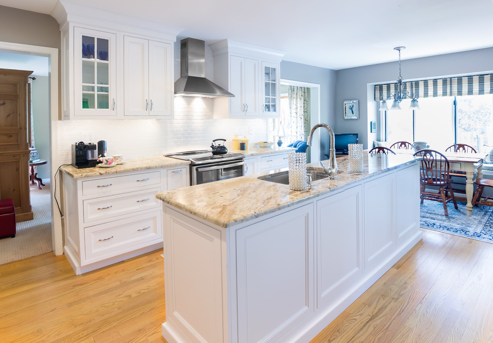 This is an example of a large transitional u-shaped eat-in kitchen in Philadelphia with an undermount sink, shaker cabinets, white cabinets, granite benchtops, white splashback, ceramic splashback, stainless steel appliances, medium hardwood floors, with island, brown floor and beige benchtop.