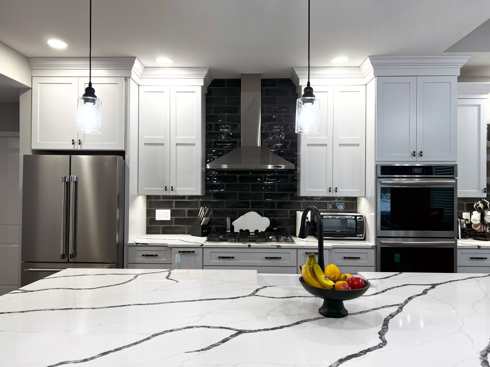 Example of a large transitional single-wall vinyl floor and beige floor eat-in kitchen design with a farmhouse sink, shaker cabinets, white cabinets, quartz countertops, black backsplash, subway tile backsplash, stainless steel appliances, an island and white countertops