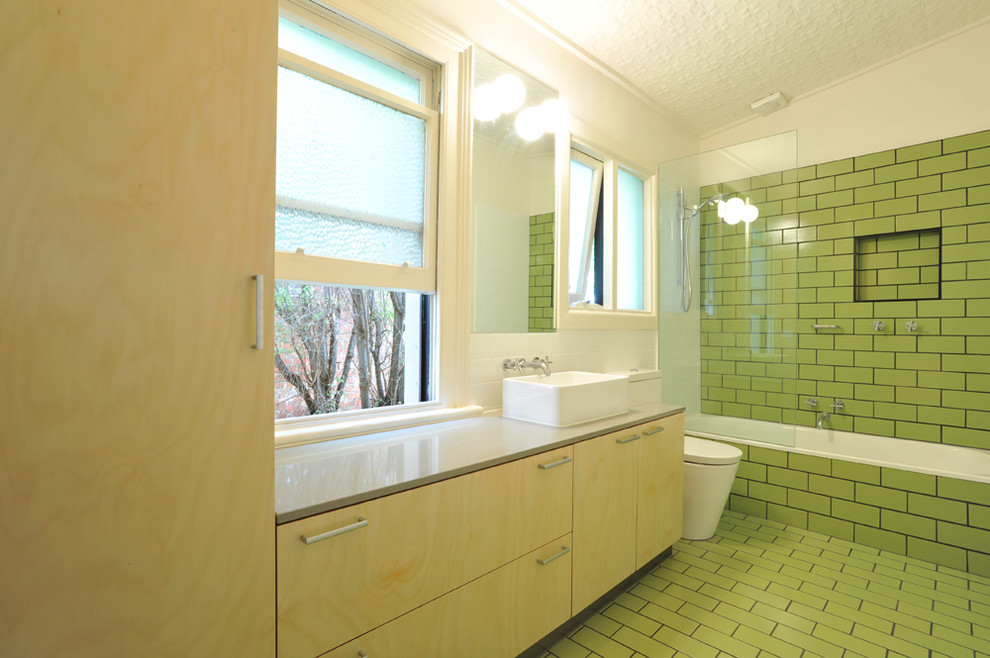 Design ideas for a small transitional kids bathroom in Melbourne with flat-panel cabinets, light wood cabinets, an alcove tub, a shower/bathtub combo, a one-piece toilet, green tile, ceramic tile, white walls, ceramic floors, a vessel sink and engineered quartz benchtops.