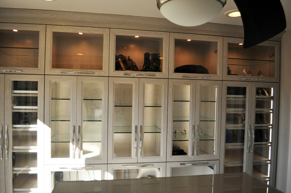 Photo of a large modern women's dressing room in Minneapolis with glass-front cabinets, grey cabinets and light hardwood floors.