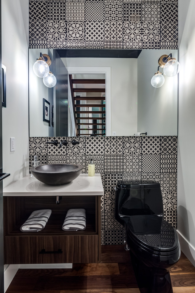 Design ideas for a contemporary powder room in Calgary with open cabinets, medium wood cabinets, a two-piece toilet, black and white tile, mosaic tile, medium hardwood floors, a vessel sink, brown floor and white benchtops.