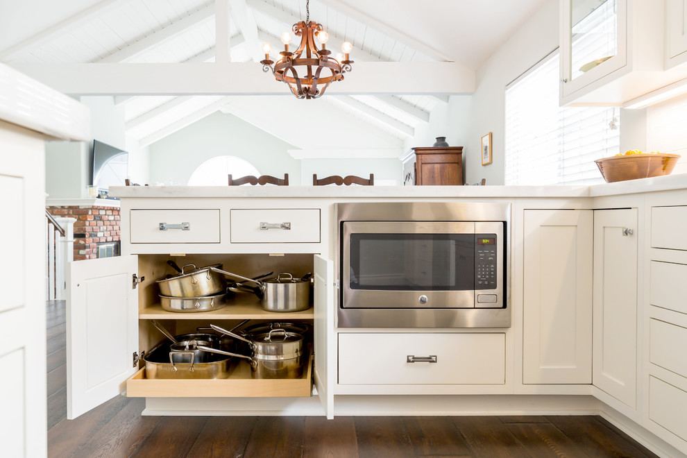 Inspiration for a mid-sized contemporary galley kitchen pantry in Los Angeles with a farmhouse sink, recessed-panel cabinets, white cabinets, quartzite benchtops, white splashback, ceramic splashback, stainless steel appliances, dark hardwood floors and a peninsula.