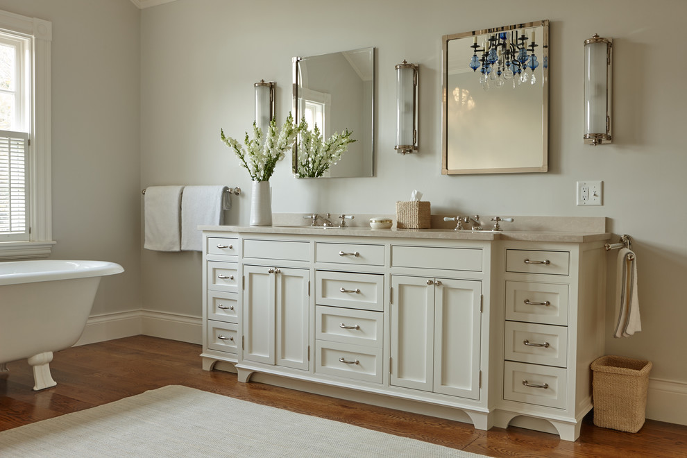 Photo of a mid-sized traditional master bathroom in Boston with raised-panel cabinets, white cabinets, a freestanding tub, an open shower, a one-piece toilet, stone slab, beige walls, medium hardwood floors, a drop-in sink and solid surface benchtops.