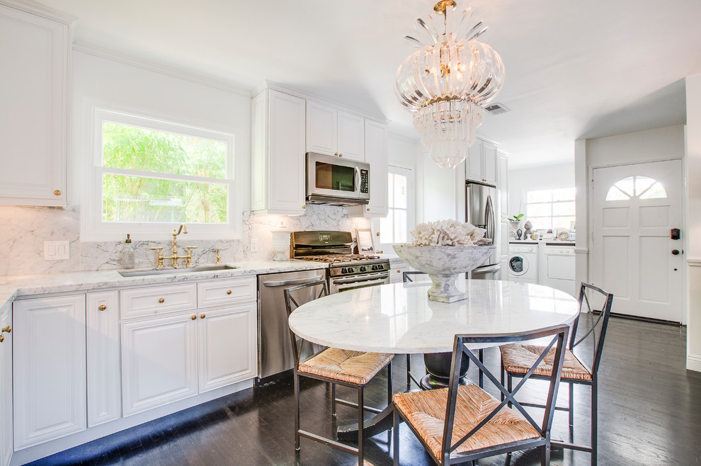 This is an example of a transitional single-wall eat-in kitchen in Los Angeles with an undermount sink, raised-panel cabinets, white cabinets, white splashback, stainless steel appliances, dark hardwood floors and no island.