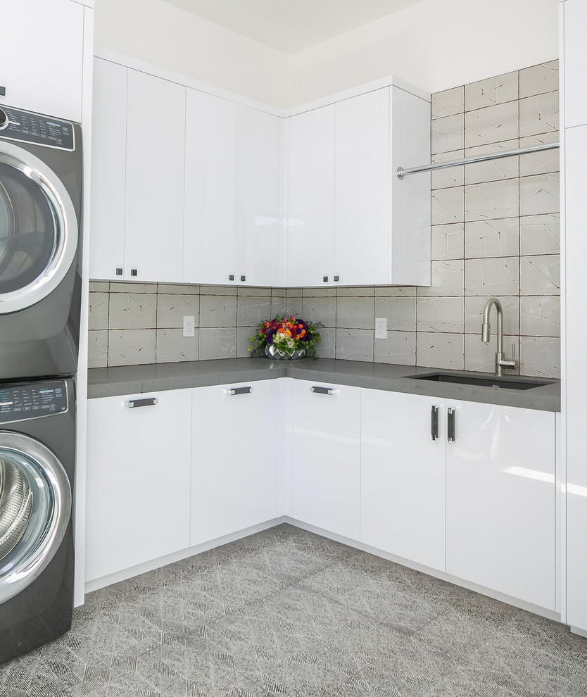 Inspiration for a contemporary l-shaped dedicated laundry room in Orange County with an undermount sink, flat-panel cabinets, white cabinets, white walls, a stacked washer and dryer, grey floor and grey benchtop.