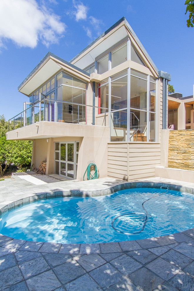This is an example of a mid-sized contemporary backyard kidney-shaped lap pool in Other with natural stone pavers.