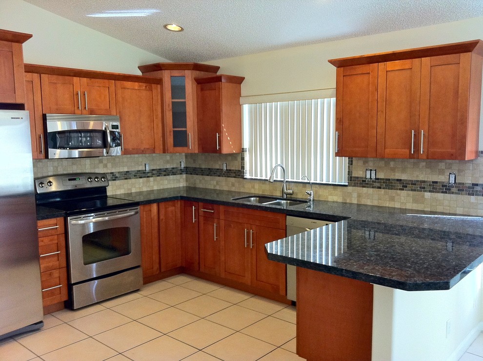 Enclosed kitchen - mid-sized transitional l-shaped porcelain tile and beige floor enclosed kitchen idea with a double-bowl sink, shaker cabinets, medium tone wood cabinets, granite countertops, beige backsplash, porcelain backsplash, stainless steel appliances, a peninsula and black countertops