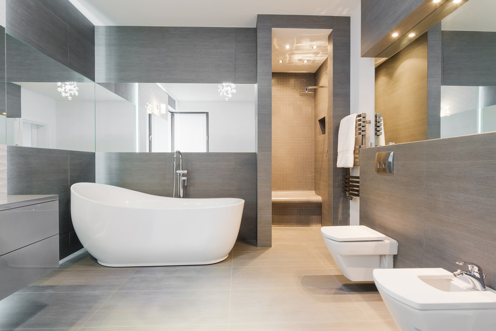 Inspiration for a master wet room bathroom in London with flat-panel cabinets, grey cabinets, a freestanding tub, a wall-mount toilet, gray tile, grey walls, grey floor and an open shower.