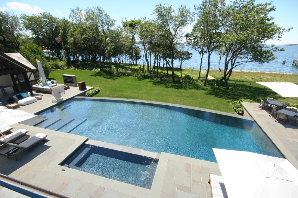 Expansive contemporary backyard rectangular infinity pool in New York with a hot tub and concrete pavers.