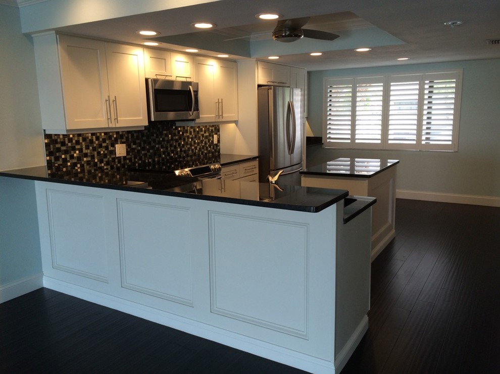 Enclosed kitchen - large transitional l-shaped dark wood floor and brown floor enclosed kitchen idea in Tampa with an undermount sink, shaker cabinets, white cabinets, solid surface countertops, multicolored backsplash, mosaic tile backsplash, stainless steel appliances and an island