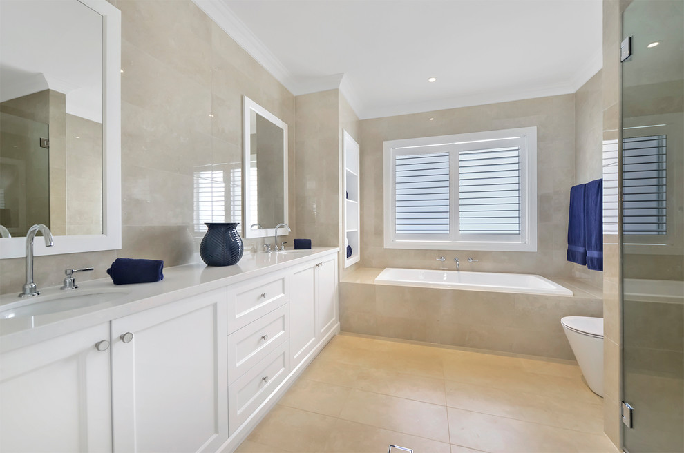 Photo of a large contemporary kids bathroom in Sydney with shaker cabinets, white cabinets, an alcove tub, a corner shower, a one-piece toilet, beige tile, limestone, beige walls, limestone floors, an undermount sink, engineered quartz benchtops, beige floor, an open shower and white benchtops.
