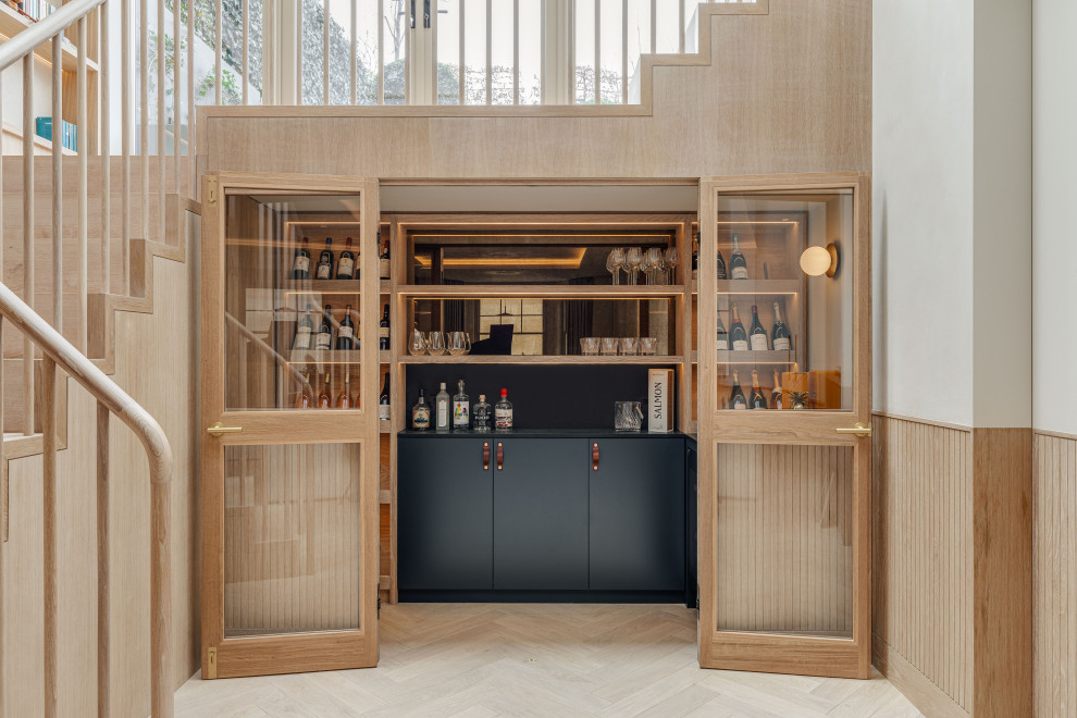 Inspiration for a contemporary home bar in London with flat-panel cabinets, grey cabinets, black splashback, light hardwood floors, beige floor and black benchtop.