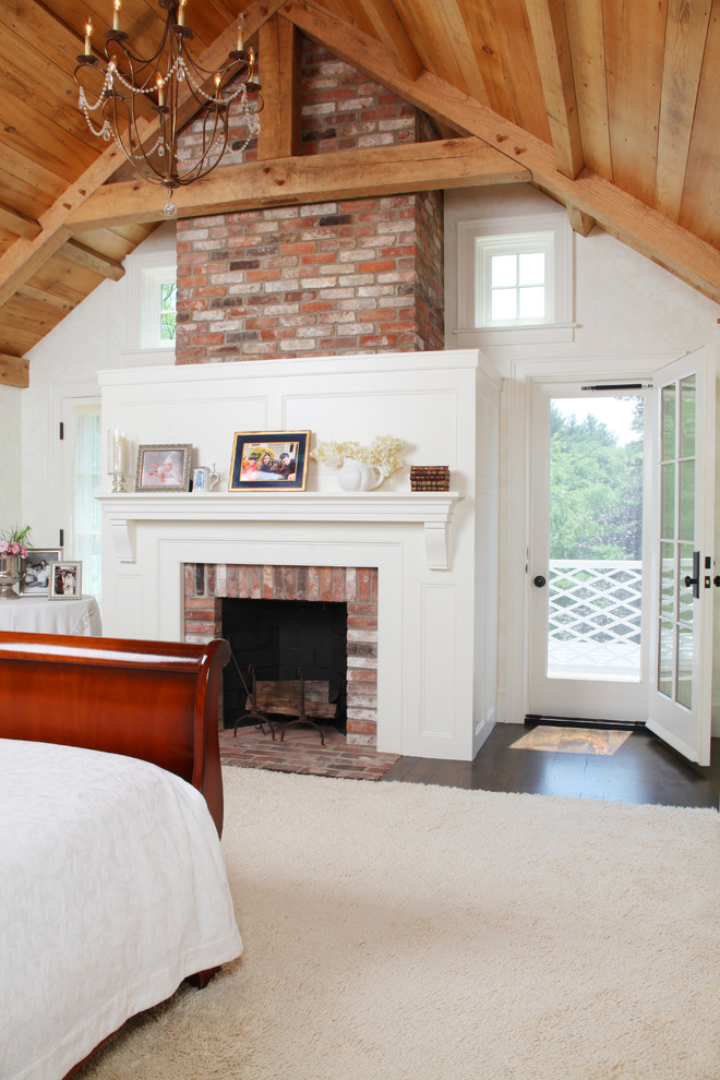 This is an example of a large country master bedroom in Boston with white walls, dark hardwood floors, a standard fireplace, a brick fireplace surround and brown floor.