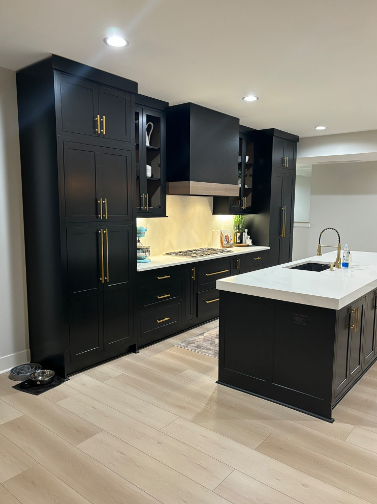 Inspiration for a large contemporary l-shaped eat-in kitchen in Detroit with a single-bowl sink, flat-panel cabinets, black cabinets, quartz benchtops, white splashback, engineered quartz splashback, stainless steel appliances, light hardwood floors, multiple islands, white floor, white benchtop and vaulted.