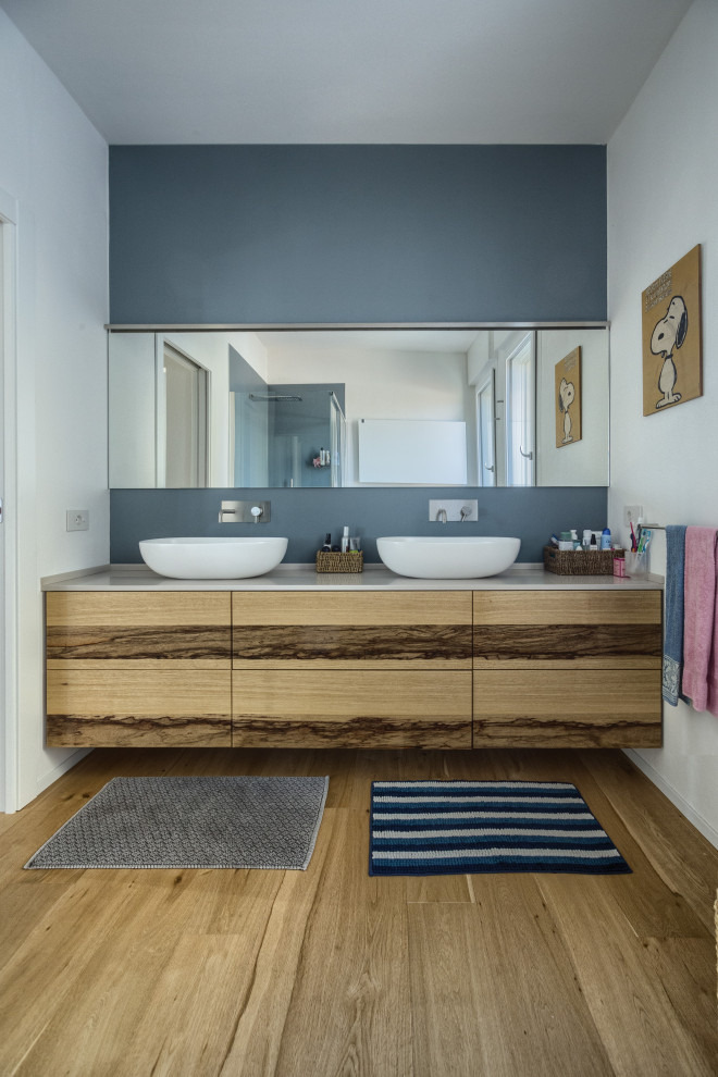 Immagine di una stanza da bagno padronale minimalista di medie dimensioni con ante lisce, ante in legno chiaro, doccia ad angolo, WC sospeso, piastrelle blu, piastrelle in gres porcellanato, pareti bianche, parquet chiaro, lavabo sospeso, porta doccia a battente, top bianco, due lavabi e mobile bagno sospeso
