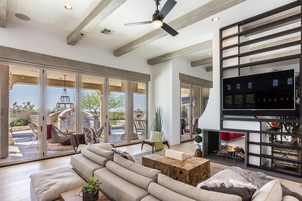 Photo of a mid-sized traditional open concept family room in Phoenix with white walls, light hardwood floors, a two-sided fireplace, a metal fireplace surround and a wall-mounted tv.
