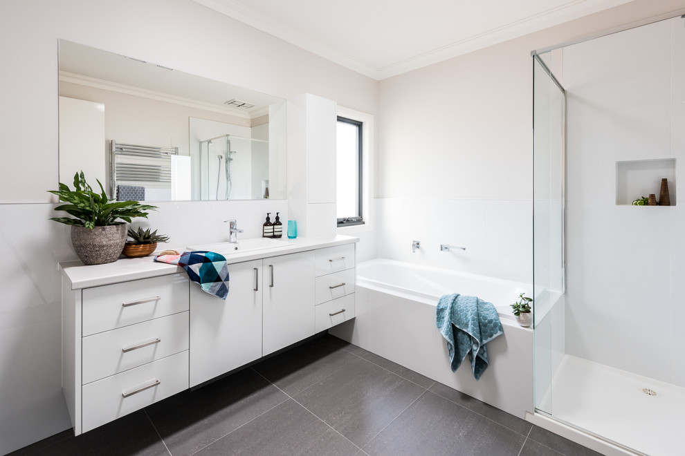 Inspiration for a mid-sized contemporary master bathroom in Melbourne with flat-panel cabinets, white cabinets, a drop-in tub, an alcove shower, white tile, porcelain tile, white walls, porcelain floors, a drop-in sink, engineered quartz benchtops, grey floor, a hinged shower door and white benchtops.