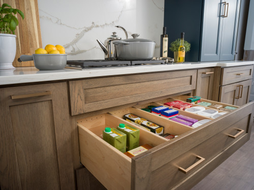 Full-extension kitchen cabinet drawer with dividers organizing pantry items beneath the cooktop; shaker wood fronts and white quartz backsplash
