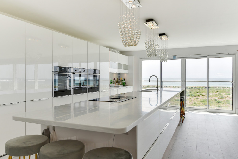 Design ideas for an expansive modern single-wall open plan kitchen in Sussex with an integrated sink, flat-panel cabinets, white cabinets, quartzite benchtops, multi-coloured splashback, glass sheet splashback, black appliances, laminate floors, with island, grey floor and white benchtop.