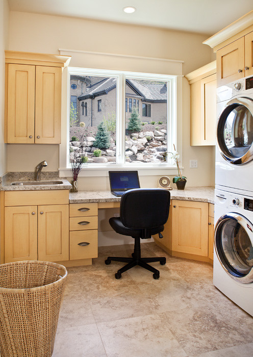 Inspiration for a mid-sized traditional l-shaped utility room in Salt Lake City with an undermount sink, shaker cabinets, light wood cabinets, granite benchtops, beige walls, ceramic floors and a stacked washer and dryer.
