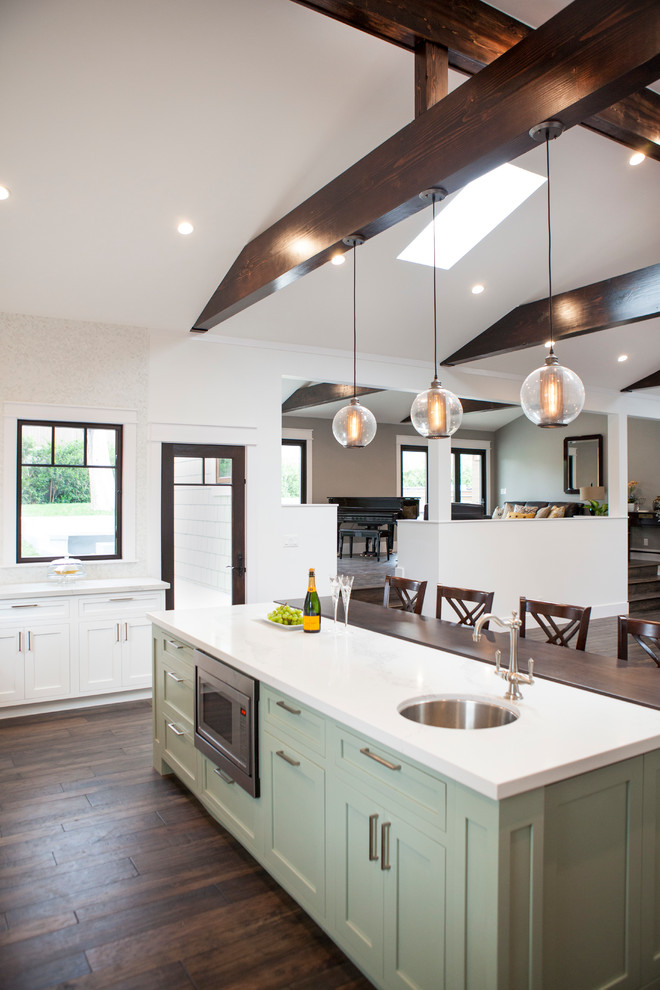 Design ideas for a large arts and crafts l-shaped eat-in kitchen in Los Angeles with a farmhouse sink, shaker cabinets, white cabinets, quartz benchtops, white splashback, glass sheet splashback, stainless steel appliances, medium hardwood floors, with island and brown floor.