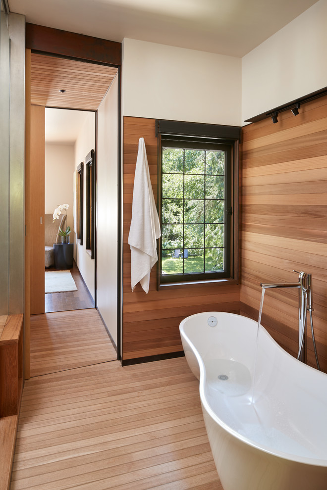 This is an example of a contemporary master bathroom in Seattle with stainless steel benchtops, a freestanding tub, brown walls, medium hardwood floors and beige floor.