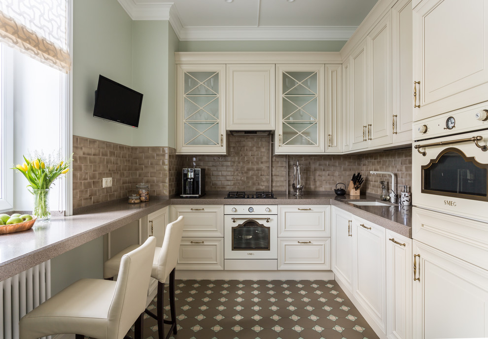 Mid-sized transitional u-shaped separate kitchen in Moscow with a single-bowl sink, raised-panel cabinets, beige cabinets, brown splashback, ceramic splashback, no island, brown floor, brown benchtop, solid surface benchtops, white appliances and porcelain floors.