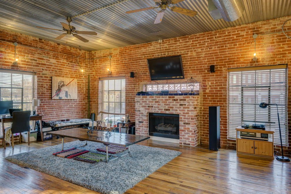 Large industrial open concept living room in Austin with red walls, medium hardwood floors, a standard fireplace, a brick fireplace surround and a wall-mounted tv.